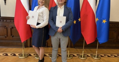 Dwoje pracowników WIOŚ w Łodzi z zaświadczeniami ukończenia służby przygotowawczej na tle flag polskich i unijnych