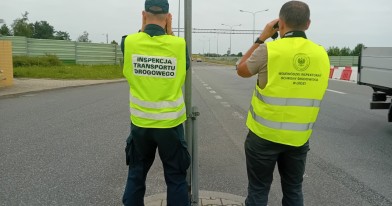 Inspektor Inspekcji Transportu Drogowego oraz Inspektor Ochrony Środowiska, stojący przy drodze krajowej  podczas czynności kontrolnych